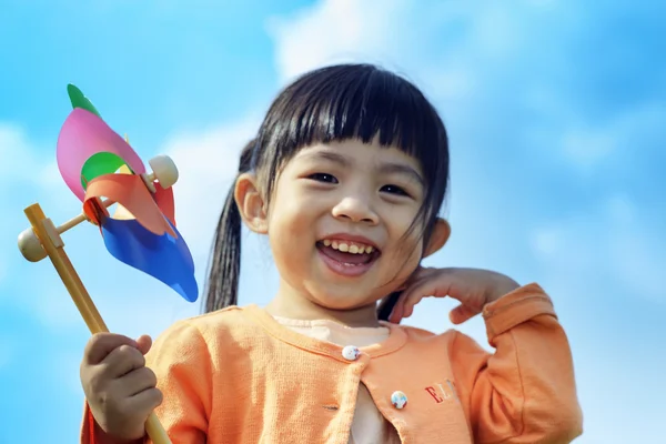 Cute little girl on grass in summer day holds windmill — Stock Photo, Image