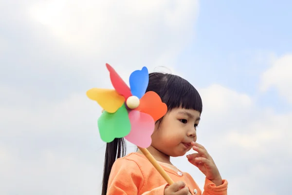 Bonito menina no grama no verão dia detém moinho de vento — Fotografia de Stock