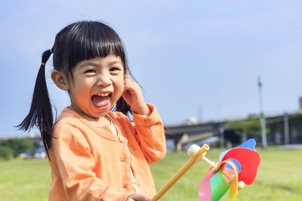 Cute little girl on grass in summer day holds windmill — Stock Photo, Image