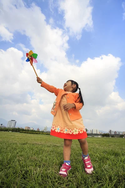 Cute little girl on grass in summer day holds windmill — Stock Photo, Image