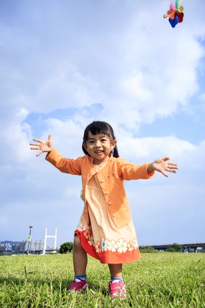 Cute little girl on grass in summer day holds windmill — Stock Photo, Image