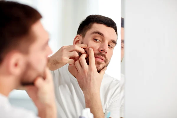 Man squeezing pimple at bathroom mirror — Stock Photo, Image