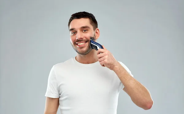 Homem sorrindo barba de barbear com aparador sobre cinza — Fotografia de Stock