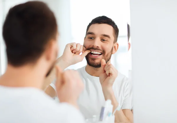 Man with dental floss cleaning teeth at bathroom — Stock Photo, Image