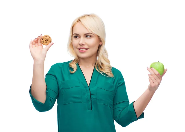 Mulher sorrindo escolher entre maçã e biscoito — Fotografia de Stock