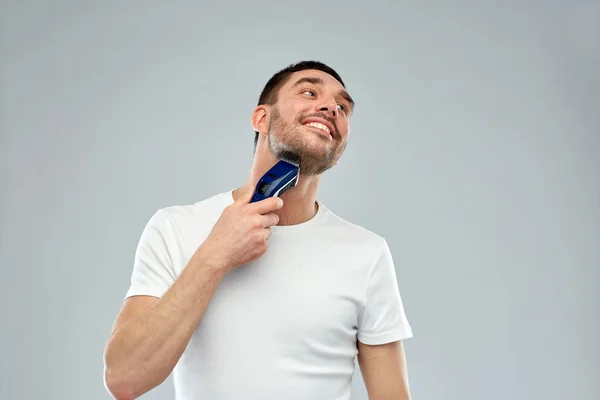 Sonriente hombre afeitando la barba con trimmer sobre gris — Foto de Stock