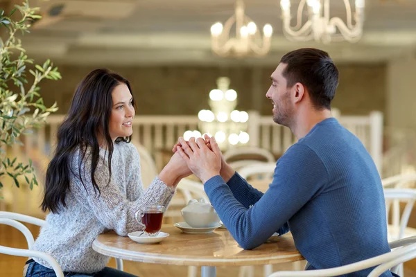 Happy couple with tea holding hands at restaurant — Stock Photo, Image