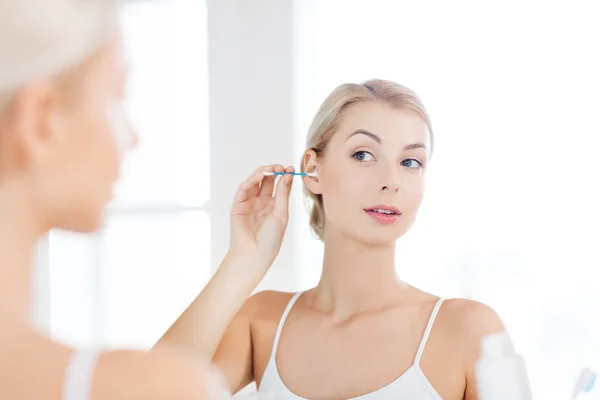 Женщина чистит ухо ватным тампоном в ванной комнате — стоковое фото