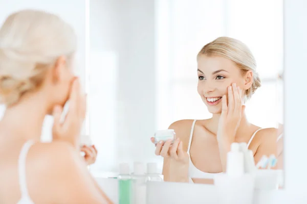 Mujer feliz aplicando crema a la cara en el baño — Foto de Stock