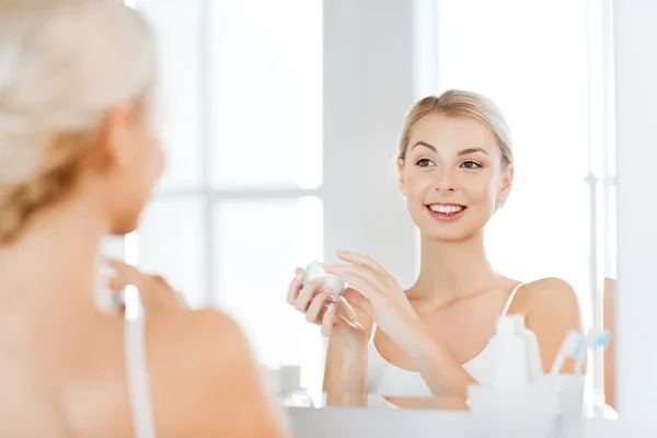 Mulher feliz aplicando creme no rosto no banheiro — Fotografia de Stock