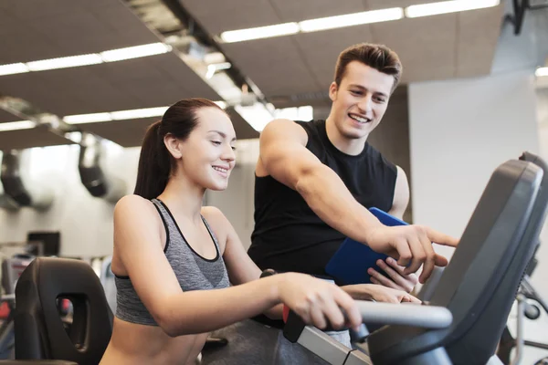 Mujer feliz con entrenador en bicicleta estática en el gimnasio —  Fotos de Stock