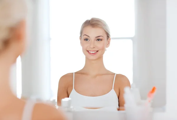 Happy young woman looking to mirror at bathroom — Stock Photo, Image