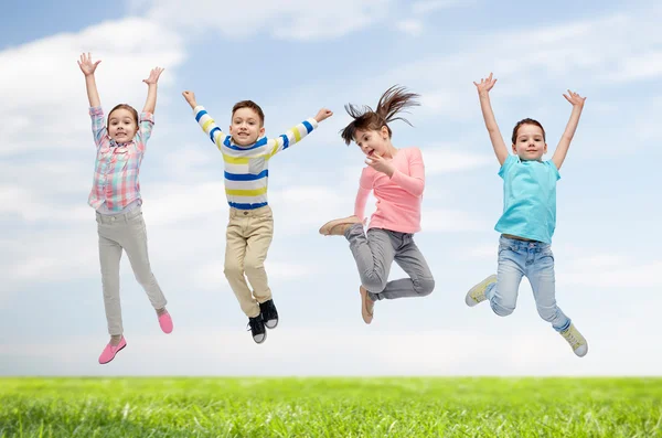 Niños felices saltando en el aire sobre el cielo y la hierba — Foto de Stock