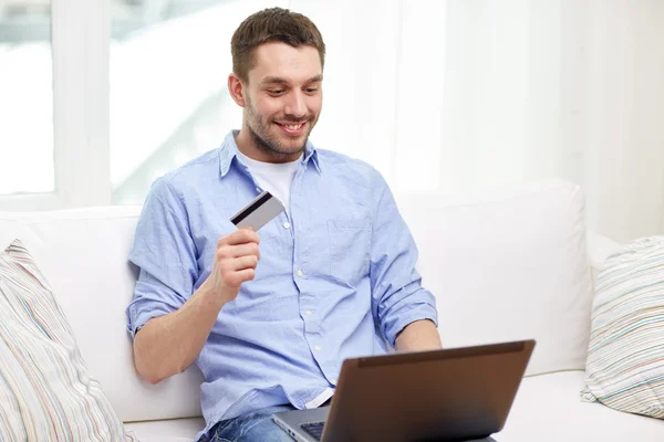 Uomo sorridente con computer portatile e carta di credito a casa — Foto Stock