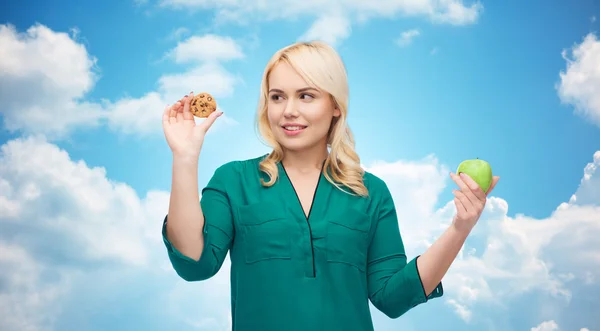 Mulher sorrindo escolher entre maçã e biscoito — Fotografia de Stock