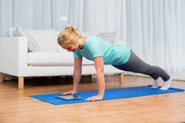 Woman with tablet pc doing plank exercise at home — Stockfoto