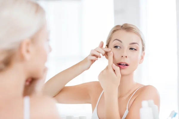 Woman squeezing pimple at bathroom mirror — Stock Photo, Image