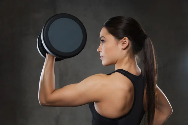 Mujer joven flexionando los músculos con pesas en el gimnasio —  Fotos de Stock