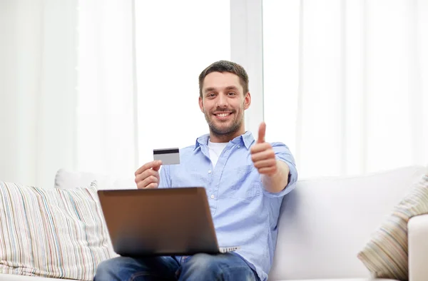 Мужчина с ноутбуком и кредитной картой, показывающей вверх большие пальцы — стоковое фото