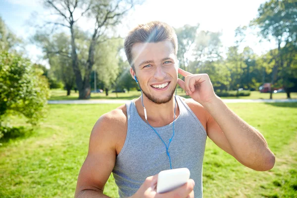 イヤホンと公園でスマート フォンを持つ幸せな男 — ストック写真