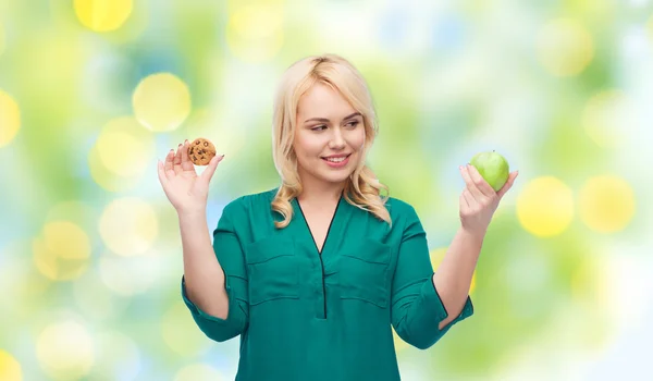 Mulher sorrindo escolher entre maçã e biscoito — Fotografia de Stock