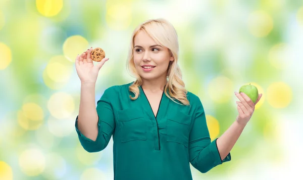 Mulher sorrindo escolher entre maçã e biscoito — Fotografia de Stock