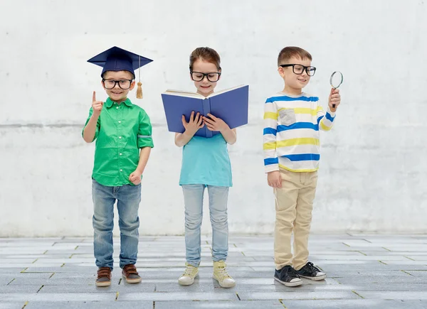 Dzieci w okularach z książki, obiektyw i licencjat kapelusz — Zdjęcie stockowe