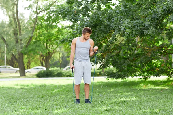 Mladý muž, cvičení s expandér v letním parku — Stock fotografie