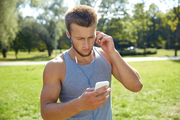 Mladý muž s sluchátka a smartphone v parku — Stock fotografie