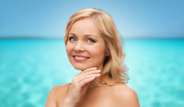 Sonriente mujer de mediana edad tocando la cara sobre el mar —  Fotos de Stock