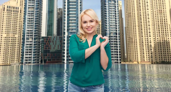 Smiling young woman in shirt showing heart shape — Stock Photo, Image