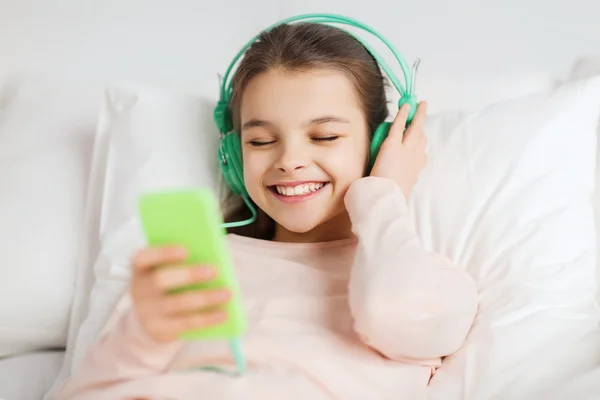 快乐的女孩躺在床上与智能手机在家里 — 图库照片