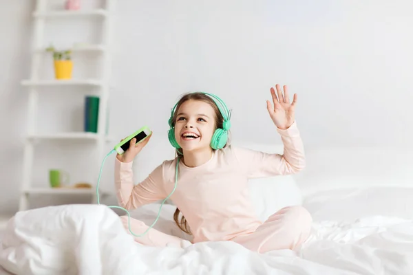 Mädchen sitzt mit Smartphone und Kopfhörer im Bett — Stockfoto