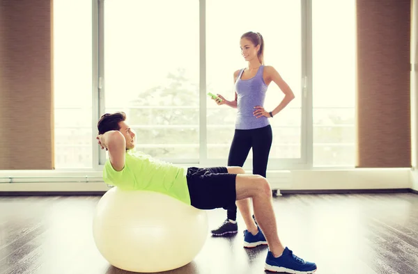 Sonriente hombre y mujer con bola de ejercicio en el gimnasio —  Fotos de Stock