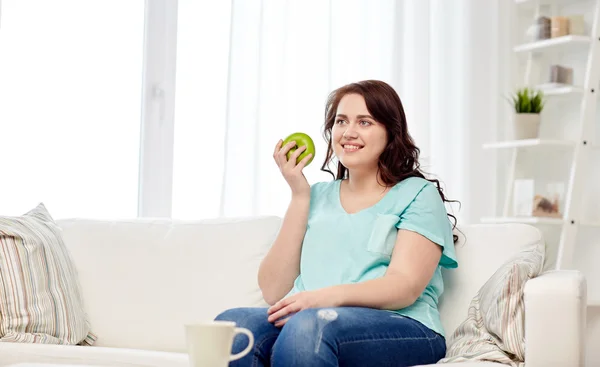 Happy plus size woman eating green apple at home — Stock Photo, Image