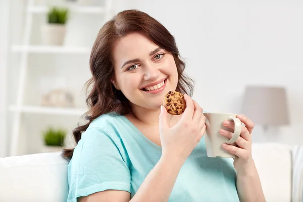 Feliz mulher plus size com copo e biscoito em casa — Fotografia de Stock