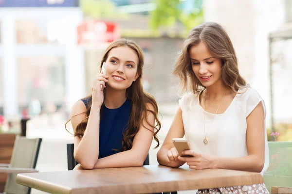 Mujeres jóvenes felices con teléfonos inteligentes en la cafetería al aire libre — Foto de Stock