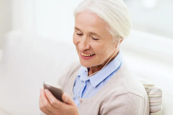 Senior vrouw met smartphone en oortelefoons thuis — Stockfoto