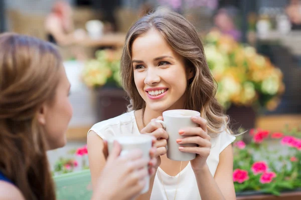 Smiling young women with coffee cups at cafe — Stock Photo, Image