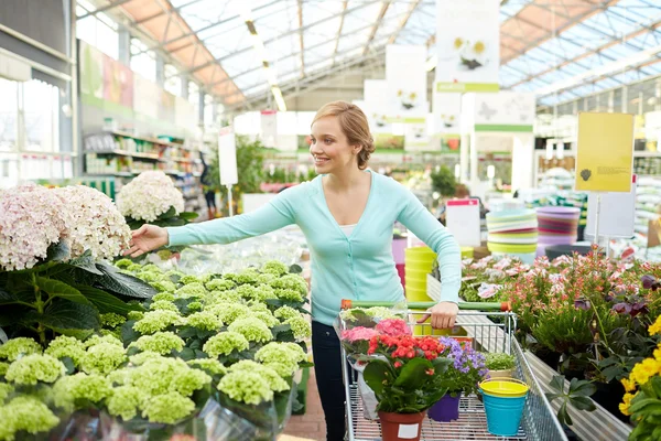 Glad kvinna med kundvagn och blommor i butik — Stockfoto