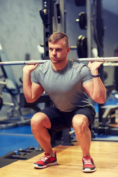Joven hombre flexionando los músculos con barra en el gimnasio —  Fotos de Stock
