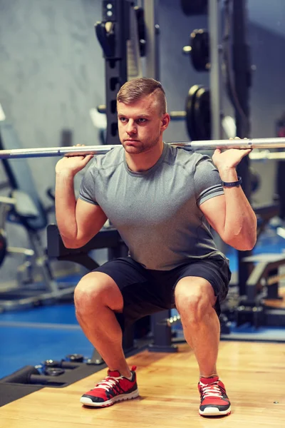 Jonge man flexen spieren met lange halter in de sportschool — Stockfoto