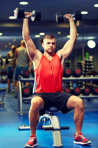 Young man with dumbbells flexing muscles in gym — Stock Photo, Image