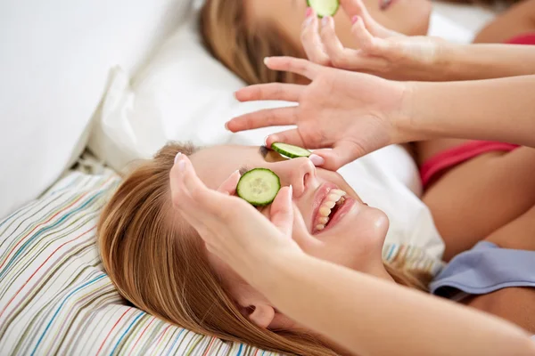 Mujeres jóvenes felices con máscara de pepino acostado en la cama — Foto de Stock
