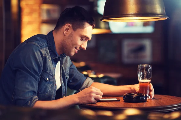 Hombre con teléfono inteligente y cerveza mensajes de texto en el bar —  Fotos de Stock