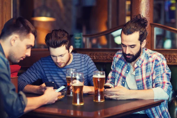 Mannlige venner med smarttelefoner som drikker øl på bar – stockfoto