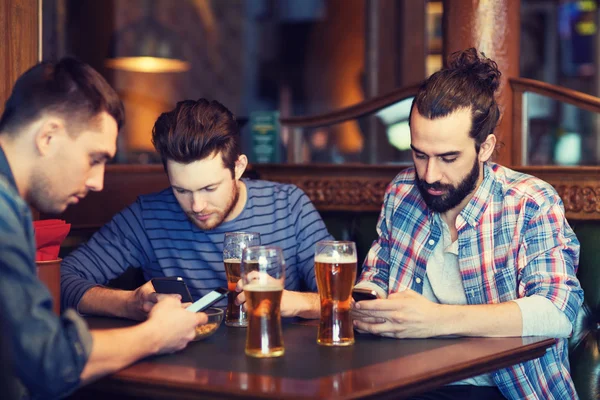 Manliga vänner med smartphones dricka öl på bar — Stockfoto