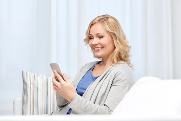 Mujer sonriente con mensajes de texto de teléfonos inteligentes en casa —  Fotos de Stock