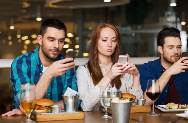 Друзья со смартфонами обедают в ресторане — стоковое фото