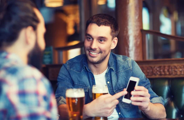 Amigos masculinos com smartphone bebendo cerveja no bar — Fotografia de Stock